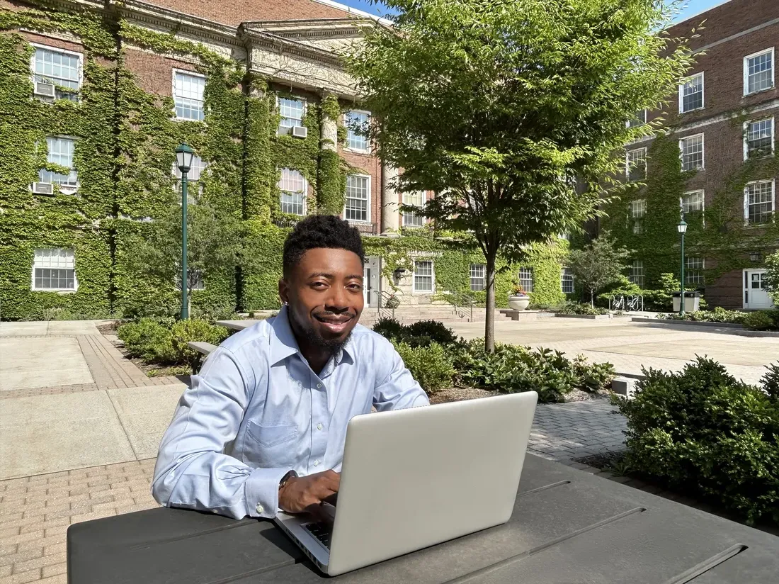 Student sitting outside while looking at a computer.